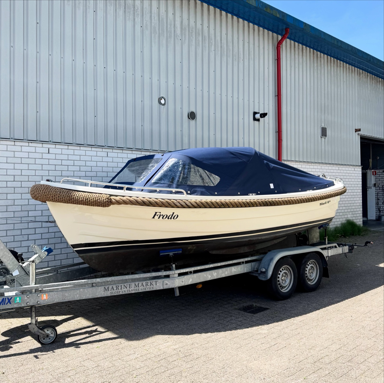 Maril 625 sloep Frodo met crèmekleurige romp en donkerblauwe buiskap met schuin aflopend achterzeil, op de trailer voor het atelier van Victorie Zeilmakerij in Loosdrecht